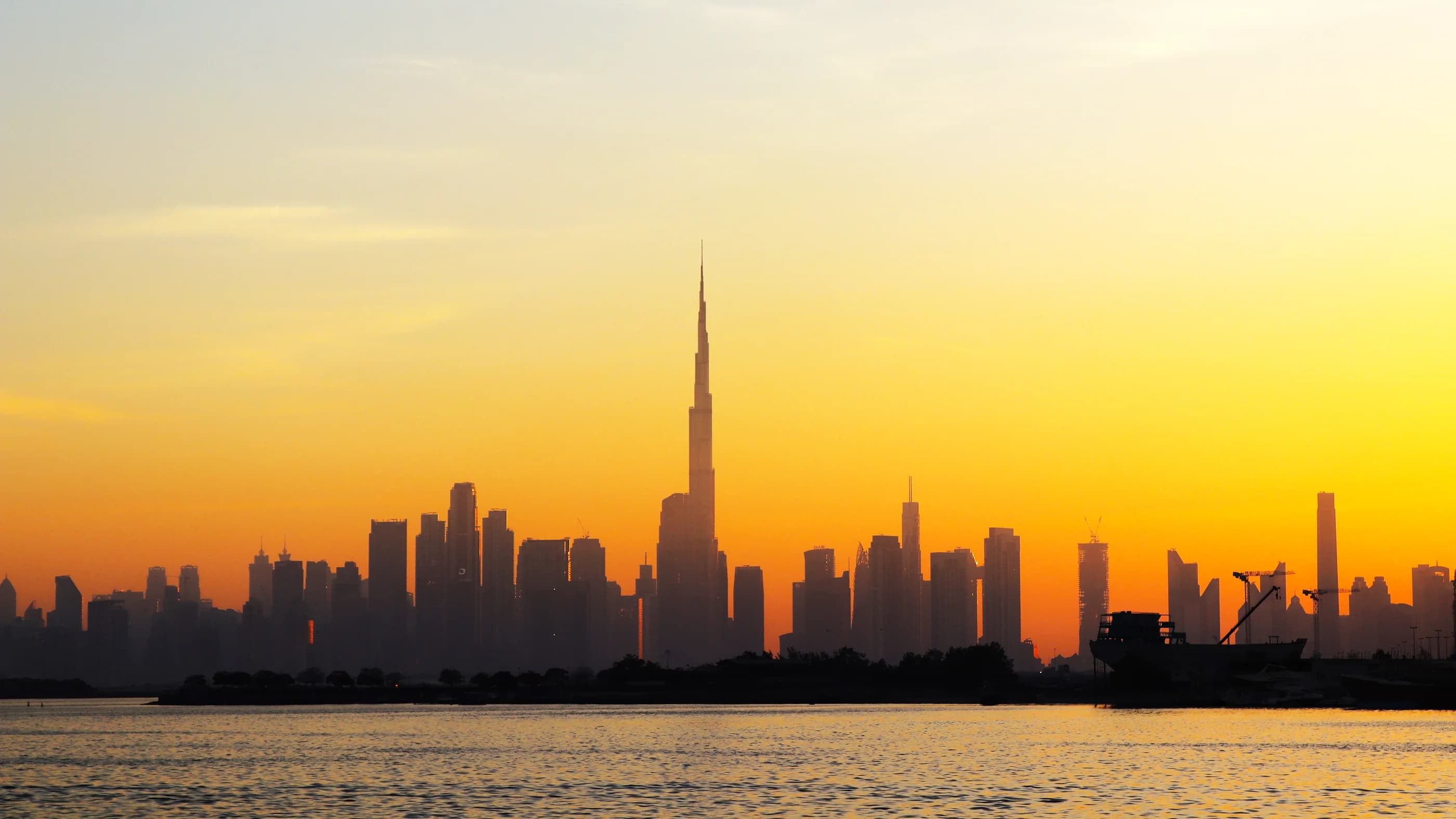 Dubai skyline and Burj Khalifa seen across the water from Dubai Creek Harbour at sunset.