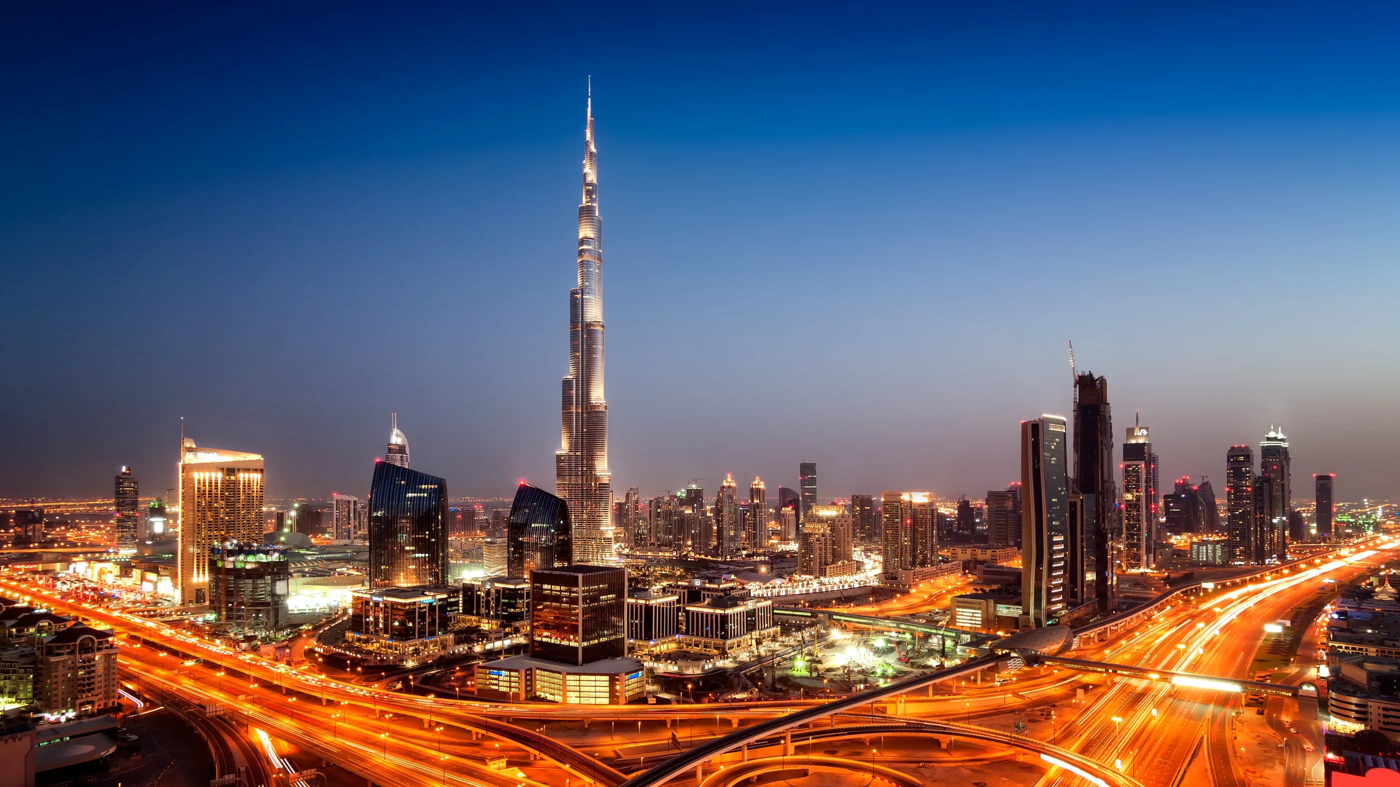 Downtown Dubai at dusk: the Burj Khalifa above the city’s towers and lit highway interchanges.